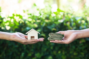 Hand holding home model change to money with green nature as ba