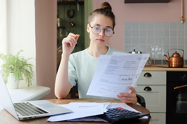 Attractive woman sits at kitchen table filling application form, calculating expenses